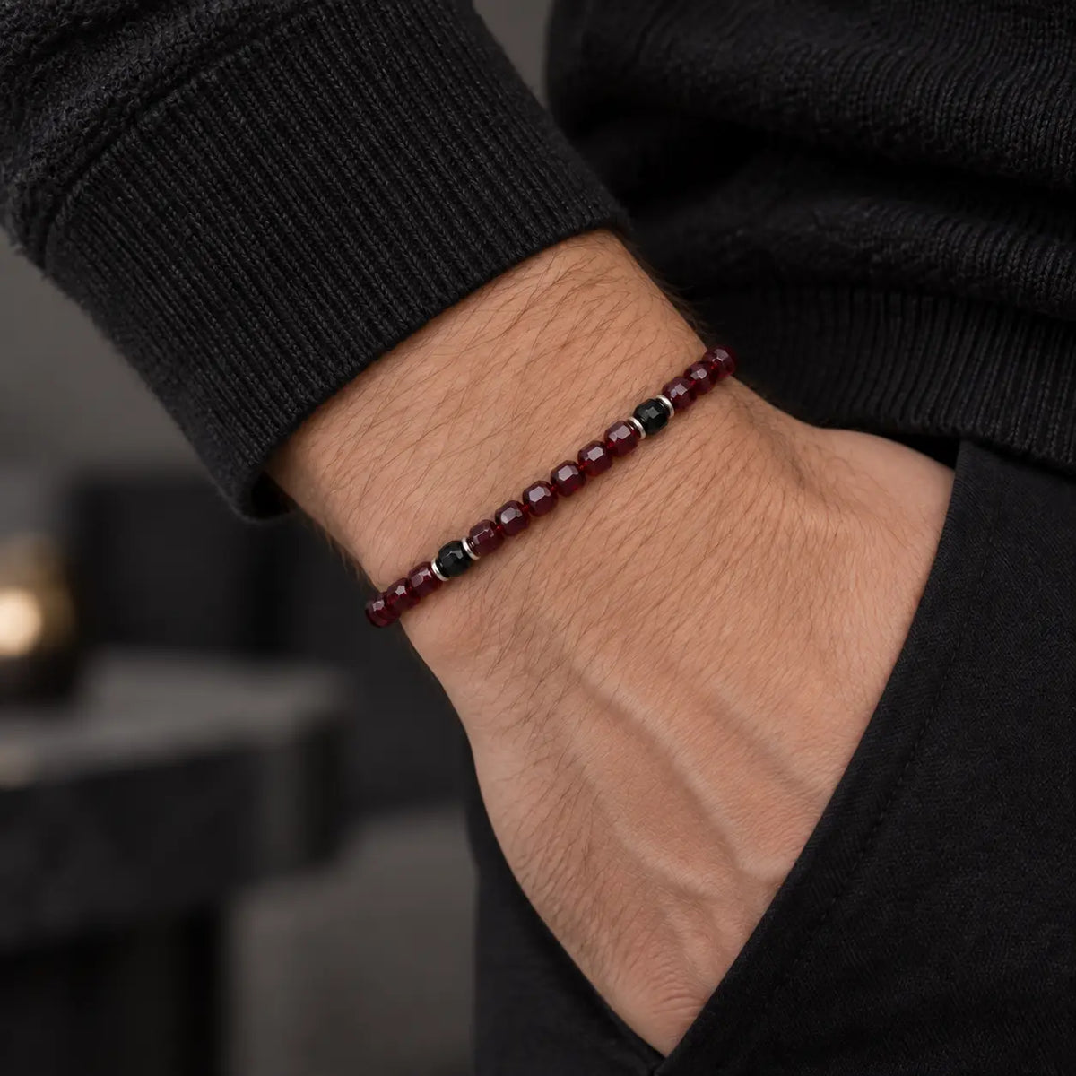 Slim natural garnet and black obsidian bracelet worn on a man's wrist.